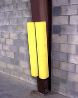 Two yellow foam covers on vertical metal poles against a brick wall.
