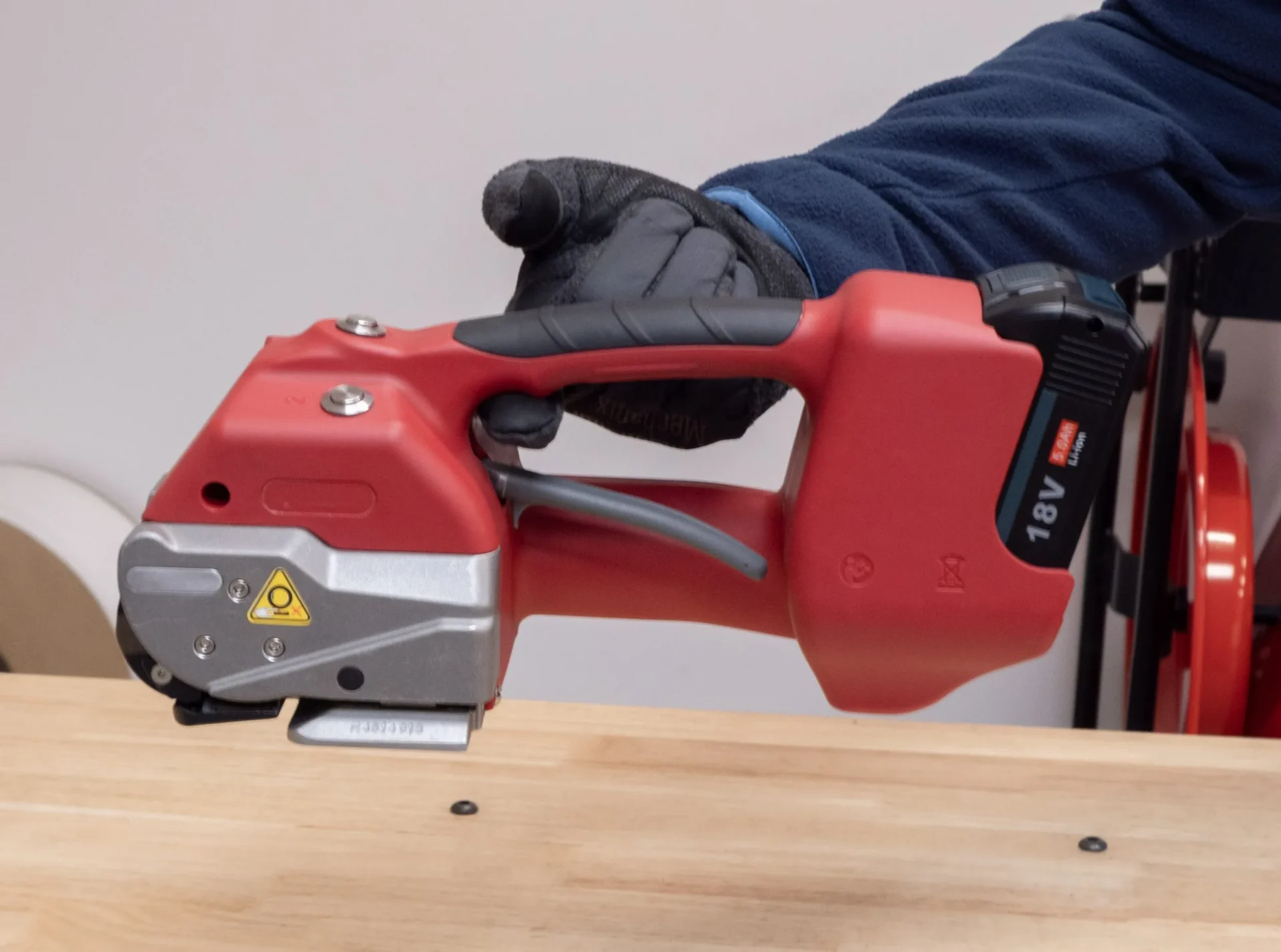 Gloved hand holding red power tool on wood